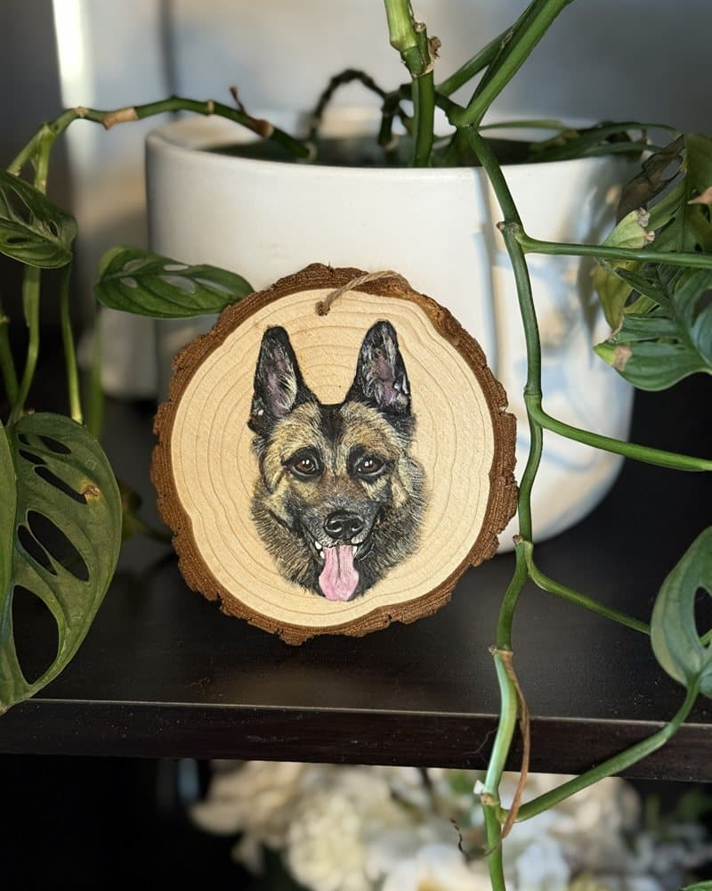 Hand-painted German shepherd on a wood round ornament beside a houseplant